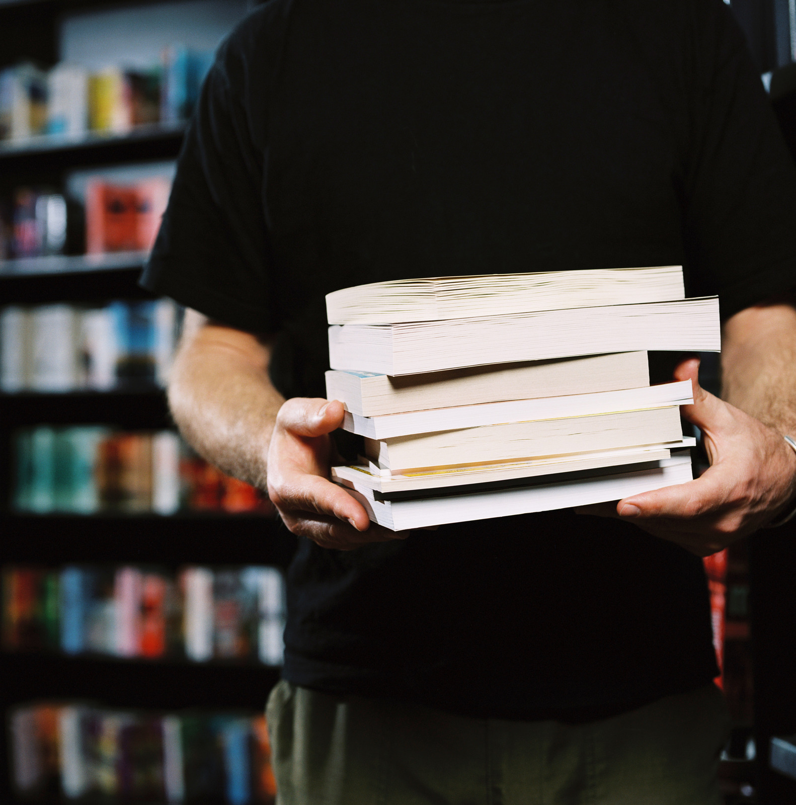 Person holding a stack of books in a library