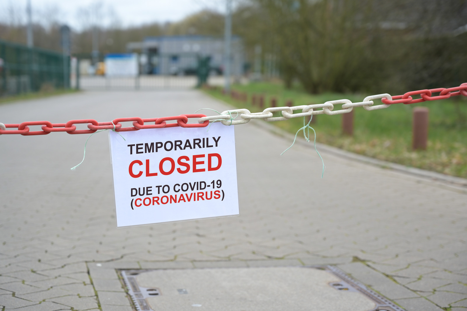 Red white chain barrier and sign with text Temporarily Closed due to Covid-19 Coronavirus, in front of a blurred company, countrywide pandemic lock down, copy space,