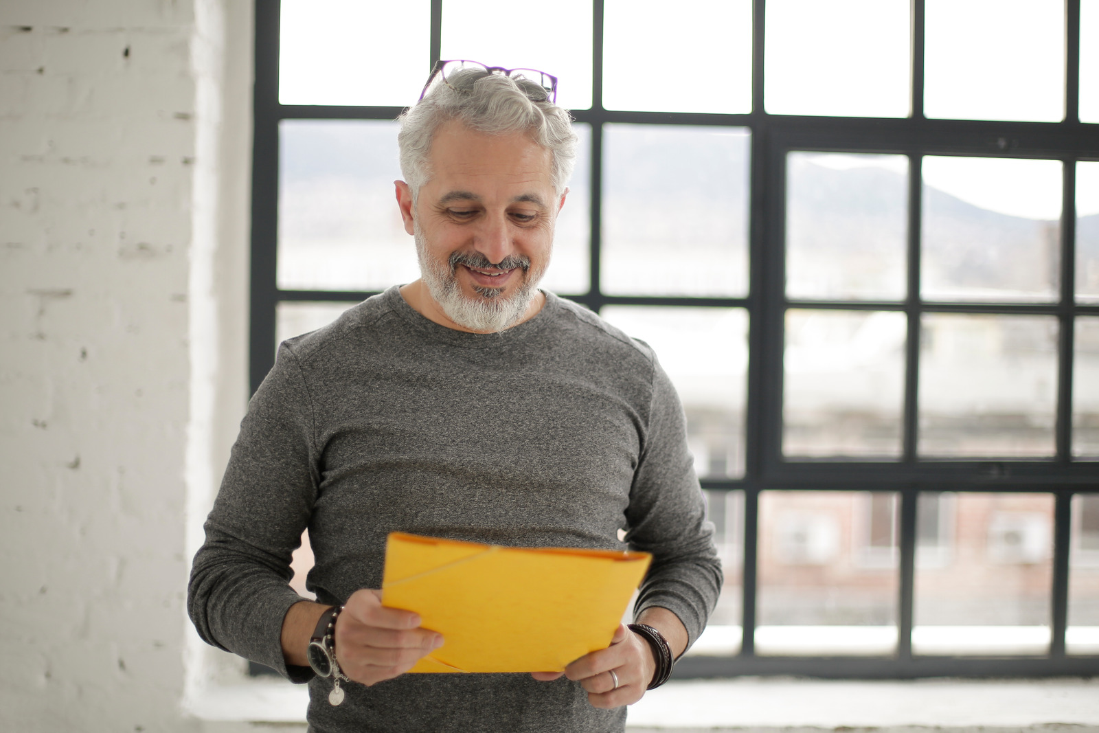 Canva – Cheerful mature male employee holding documents against window in workspace